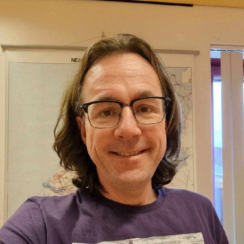 Persoon met bril, half lang jaar tot op de schouders en een paars shirt