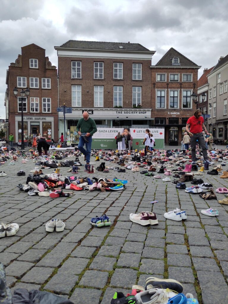 Mensen plaatsen kinderschoenen gestructureerd op de markt. Er liggen stapels schoenen die nog geplaatst moeten worden.